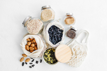 Fototapeta na wymiar Nuts, dried fruits and groats in eco cotton bags and glass jars on white table in the kitchen. Zero Waste Food Shopping. Waste-free living