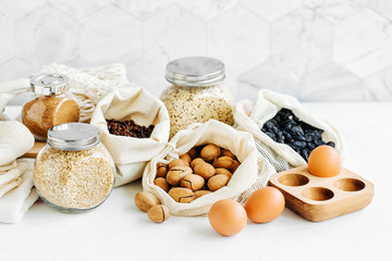 Nuts, dried fruits and  groats  in eco cotton bags and glass jars on white table in the kitchen. Zero Waste Food Shopping.  Waste-free living