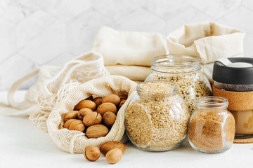 Nuts, dried fruits and  groats  in eco cotton bags and glass jars on white table in the kitchen. Zero Waste Food Shopping.  Waste-free living