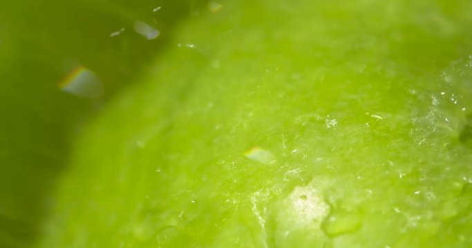 Macro close up spraying a bright, green Granny Smith apple with water in the sunshine