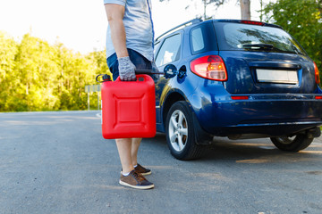 Man with a gas can on the side of the road with his car in background, close-up without a face. Driver with refuel canister of fuel on background of stalled car . Concept of empty fuel tank