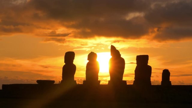 SUN FLARE SILHOUETTE: Stunning view of silhouettes of moai sculptures at stunning sunset. Beautiful golden sunbeams shine on a row of decaying ancient moai statues set along shore the of Easter Island