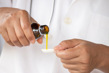 Hands of Medical person pouring syrup medicine into clear spoon