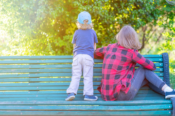 Brother and sister sitting on a bench in a park. View from the back