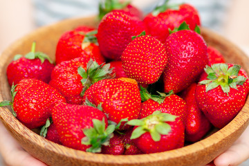 Wooden plate with strawberries in girl hand on light background, organic food concept