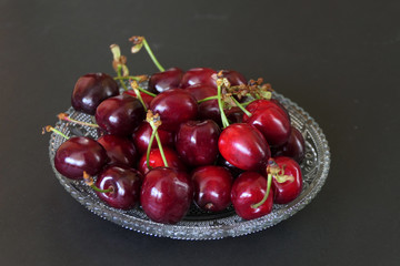 Fresh Dark Red Cherries in a Transparent Plate isolated on a Black Background