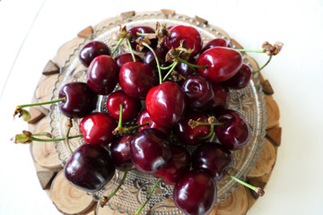 Fresh Dark Red Cherries in a Transparent Plate on a Wooden and White Background