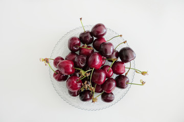 Fresh Dark Red Cherries in a Transparent Plate on a White Background