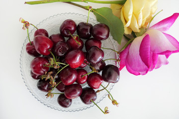 Fresh Dark Red Cherries in a Transparent Plate and Colorful Roses