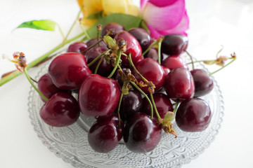 Fresh Dark Red Cherries in a Transparent Plate and Colorful Roses