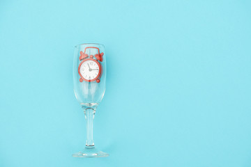 Wine glass with red alarm clock inside on blue background with copy space for text. Creative concept drinking time and wine o'clock. Top view Flat lay. Template for invitation, text, design
