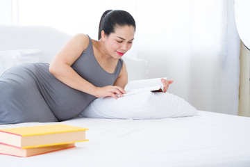 Pregnant woman reading a book on the white bed. Mental health care and pregnancy.