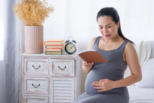 Pregnant woman reading a book and put her hand on belly. Researching information about childbirth. Mental health  care and pregnancy.