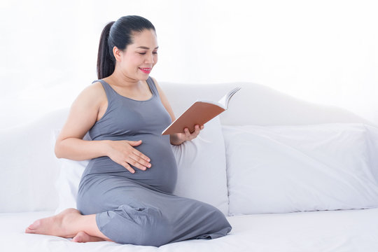 Pregnant woman reading a book, smiling happily and put your hand on belly. Mental health care and pregnancy.