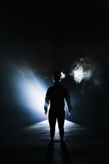 The man standing alone silhouette the darkness, abstract mysterious sci fi fantasy concept, bright light rays from behind, person alone in dark background