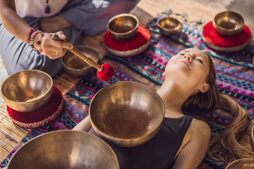 Nepal Buddha copper singing bowl at spa salon. Young beautiful woman doing massage therapy singing bowls in the Spa against a waterfall. Sound therapy, recreation, meditation, healthy lifestyle and