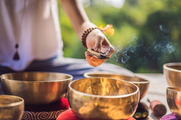 Woman playing on Tibetan singing bowl while sitting on yoga mat against a waterfall. Vintage...