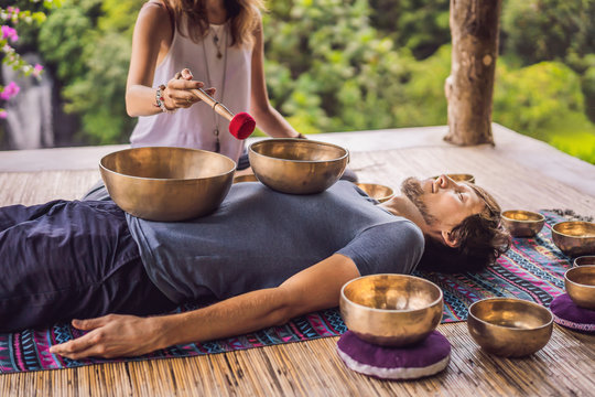 Nepal Buddha copper singing bowl at spa salon. Young beautiful man doing massage therapy singing bowls in the Spa against a waterfall. Sound therapy, recreation, meditation, healthy lifestyle and body