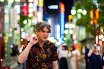 A man has an expression of not being able to hear well, while exploring the loud, vibrant city of Tokyo, Japan at night.