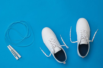White sneakers with a blue jump rope on a blue background. Sports style. Flat lay.