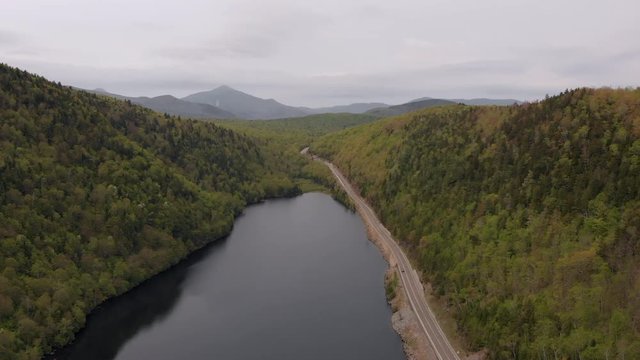 Still aerial over a lake between Northeastern mountains and country road.