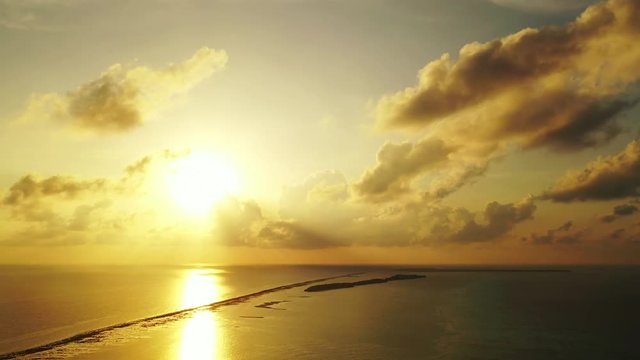 Aerial clip of a sunset in the Maldives, with the yellow rays of the sun reflection on the waters of the reef