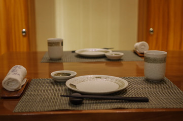 Empty japanese restaurant table setting with black chopsticks, white plates, towels, cups and gray table mats