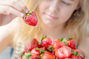 Obraz premium Wooden plate with strawberries in girl hand on light background, organic food concept