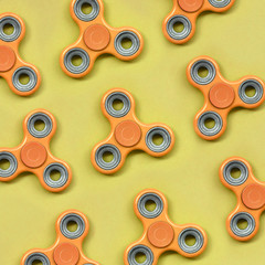 Many orange fidget spinners lies on texture background of fashion pastel orange color paper