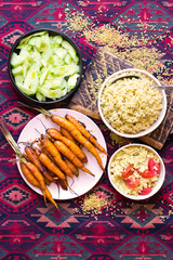 Bulgur, vegan baked carrots, vegetables salad and cooked cosucous grain in bowls in Arabic Asian style.