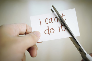 Man hand cutting paper note with scissors to remove T word from I can't do it texts. Positive...