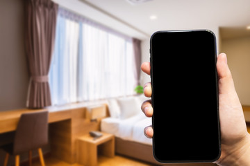 Close-up of female use Hand holding smartphone blurred images of defocused white pillow on bed decoration with light lamp in hotel bedroom interior background,Leisure and travel in the holiday concept