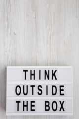 'Think outside the box' words on a lightbox on a white wooden surface, top view. Flat lay, overhead, from above. Copy space.