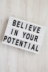 'Believe in your potential' words on a lightbox on a white wooden surface, top view. Flat lay, overhead, from above. Closeup.