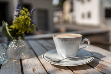 cappuccino coffe on a wooden table in front of a restaurant with blurry background