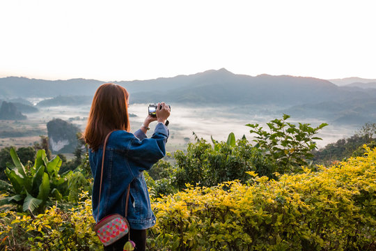 Young woman taking photos of sunrise in mountain at Phu Lung ka,Thailand