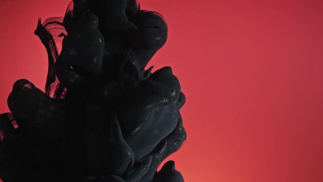 Black nacreous paint in water against red background.