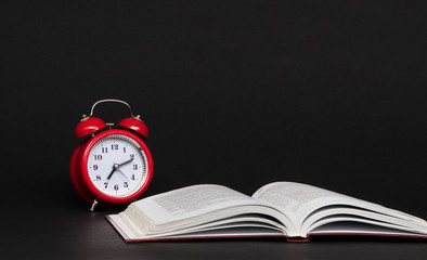 red alarm clock and open book on black background, isolated. back to school