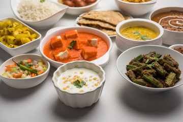 Assorted Indian food like paneer butter masala, dal, roti, rice, sabji, gulab jamun and bound raita served in bowls over moody background, selective focus