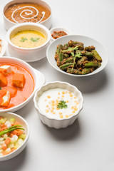 Assorted Indian food like paneer butter masala, dal, roti, rice, sabji, gulab jamun and bound raita served in bowls over moody background, selective focus