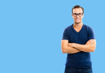 Fototapeta premium Portrait of young happy man wearing in glasses, casual smart blue clothing, with crossed arms, over blue background