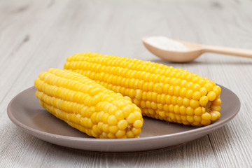 Porcelain plate with boiled corn and wooden spoon with salt on a table.