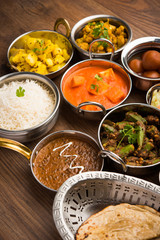 Assorted Indian food like paneer butter masala, dal, roti, rice, sabji, gulab jamun and bound raita served in bowls over moody background, selective focus