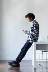 Handsome young african american man using his mobile phone while sitting on table at home.