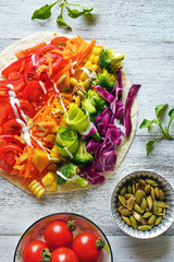 Top view of rainbow colored vegetable salad on flatbread on white table. Healthy vegetarian snack. 