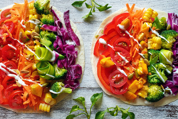 Top view of flatbread with rainbow colored vegetables on white table. 