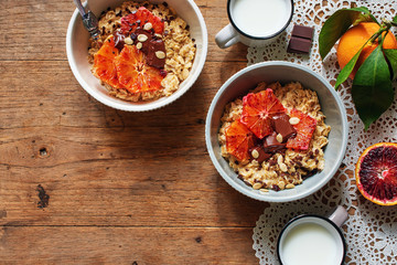 Fototapeta na wymiar Two bowls of oatmeal with red oranges and chocolate and fresh milk over wooden table. Flat lay with space for text.