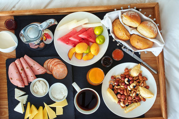 Top view of breakfast in bed in Azerbaijan hotel: fresh fruit, cheese and cold cut platter, nuts and pastry, bread basket, coffee with milk and juice. 