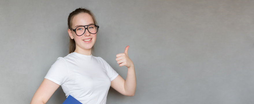  Portrait with copy space fashionable girl of the millennial generation z in white t-shirt pointing with index finger at empty space, looking at camera, isolated on gray background