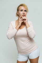 Photo portrait above the knee of a beautiful blonde woman girl with short curly hair on a white background in bright lingerie talking and showing a lot of emotions. An experienced model shows hands.